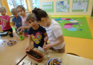 Dzieci sieją w doniczce nasiona roslin.